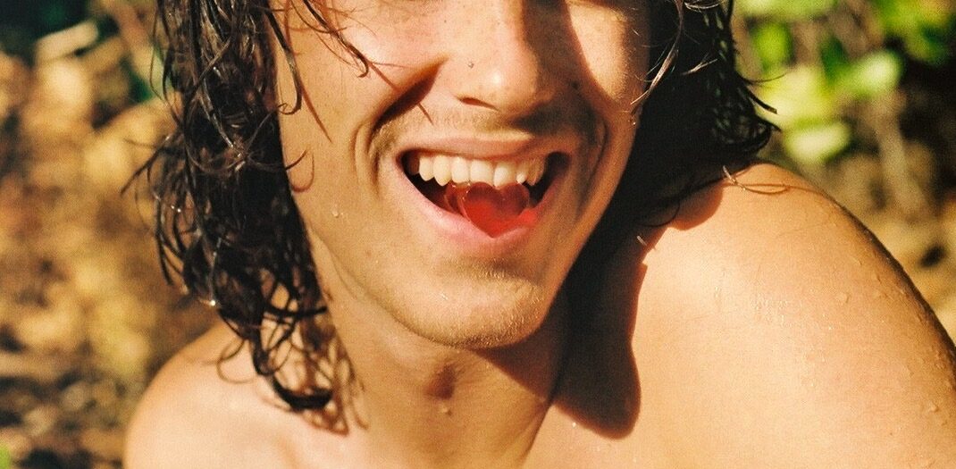 Close-up of a smiling person holding a Utopia psilocybin gummy in their mouth, representing how to take shroom gummies